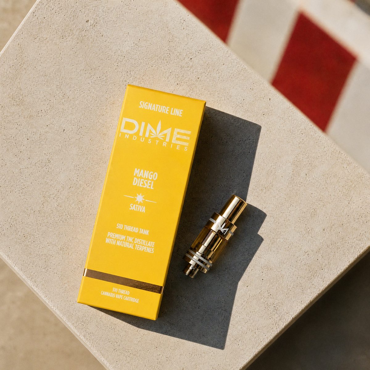 Dime Mango Diesel 510 vape cartridge and box on a sunny stone counter with red-and-white awning stripes behind